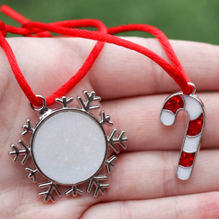 A red and white candy cane ornament and a snowflake ornament both made from breastmilk hangs on a red string are held in the palm of a hand.