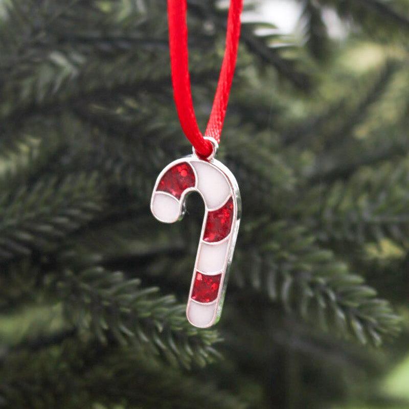 A red and white candy cane made from breastmilk hangs on a red string with a soft focus Christmas tree behind it