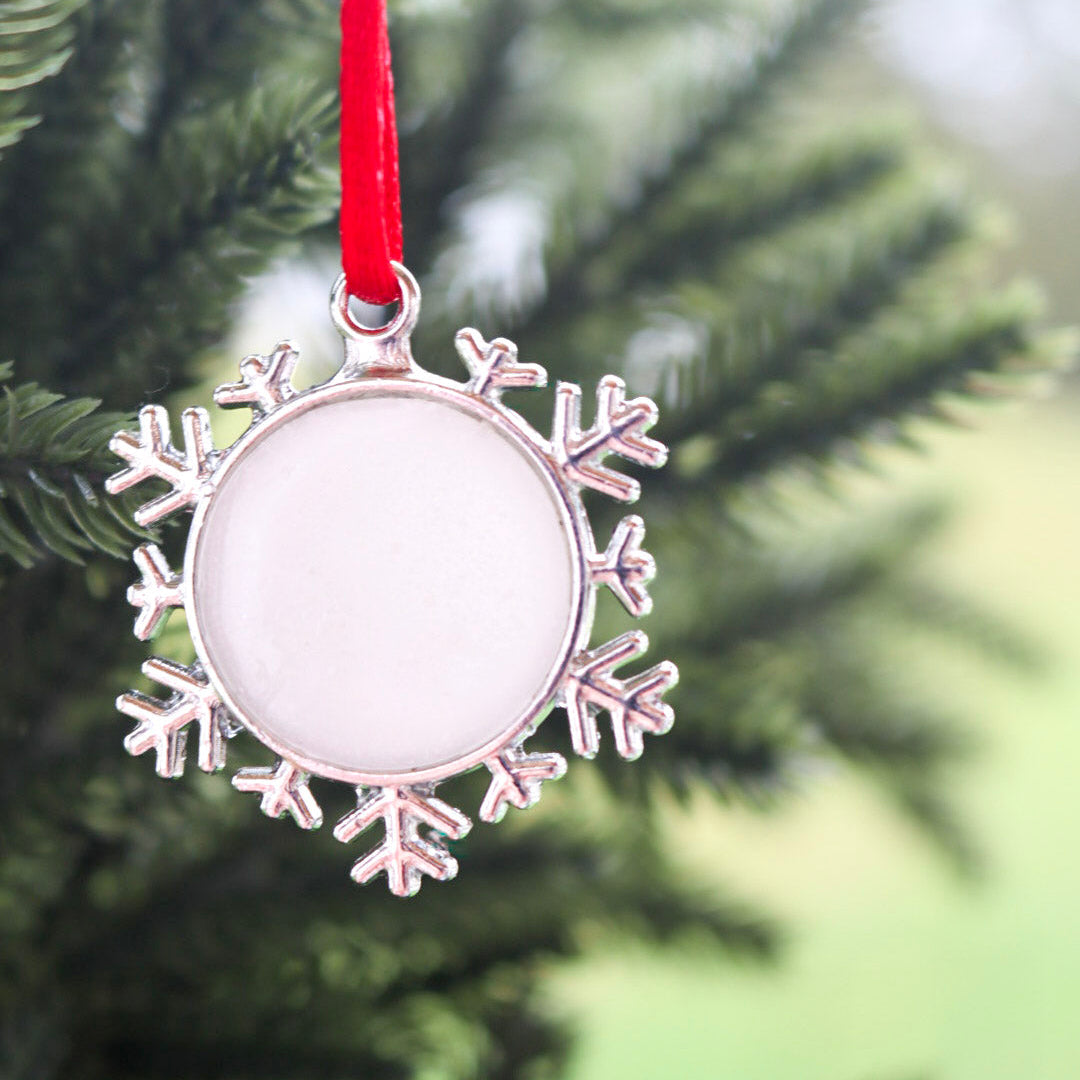 A snowflake ornament made from breastmilk hangs on a red string with a soft focus Christmas tree behind it